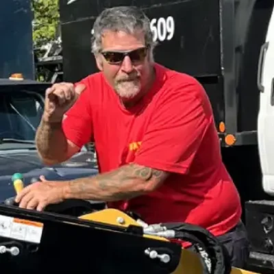 Peter Ahlert of Wayne’s Tree Service in a red shirt beside a compact tool carrier